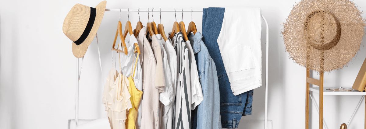 An array of summer garments including linen shirts and straw hat, hanging up on a wardrobe rail.
