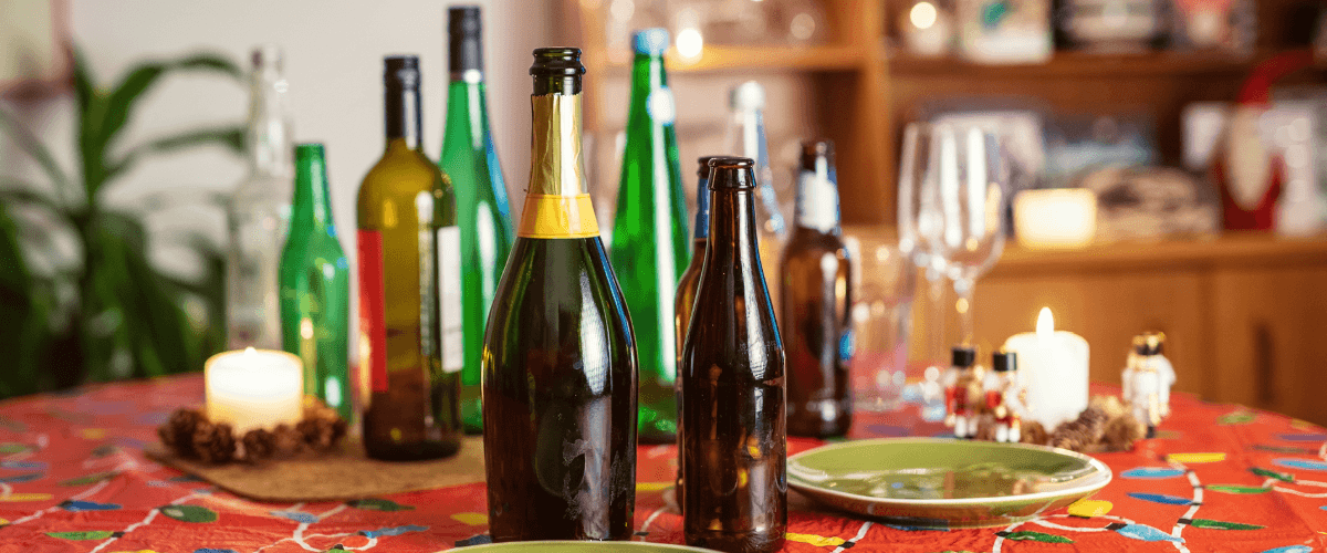 a table with a red festive tablecloth with various empty drink bottles on it. Festive candles and plates are also on the table